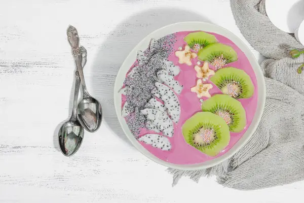 Meyve, kivi, muz ve haşhaş tohumlu Pitaya smoothie kasesi. Moda yemek, sağlıklı kahvaltı fikri. Sert ışık, karanlık gölge, beyaz ahşap zemin, üst manzara