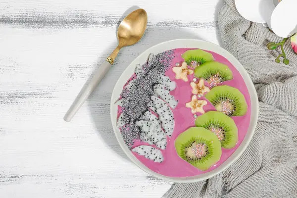 Meyve, kivi, muz ve haşhaş tohumlu Pitaya smoothie kasesi. Moda yemek, sağlıklı kahvaltı fikri. Sert ışık, karanlık gölge, beyaz ahşap zemin, üst manzara