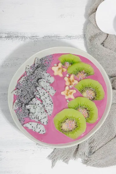 Meyve, kivi, muz ve haşhaş tohumlu Pitaya smoothie kasesi. Moda yemek, sağlıklı kahvaltı fikri. Sert ışık, karanlık gölge, beyaz ahşap zemin, üst manzara