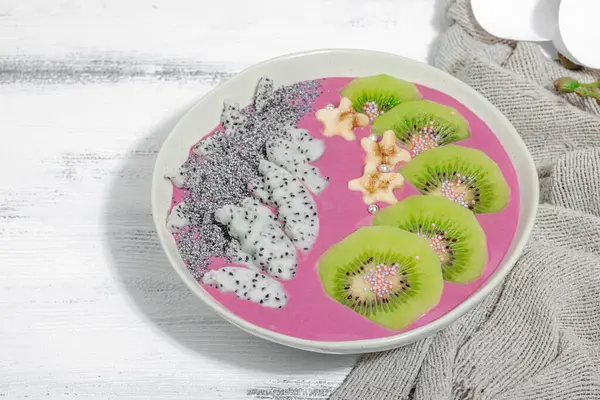 Meyve, kivi, muz ve haşhaş tohumlu Pitaya smoothie kasesi. Moda yemek, sağlıklı kahvaltı fikri. Sert ışık, karanlık gölge, beyaz ahşap zemin, kopyalama alanı