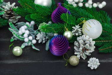 Yeni yılın kutlu olsun. Şenlikli Noel mücevherleri, her zaman yeşil dallar, kozalaklar, karlı meyveler. Siyah ahşap zemin, tebrik kartı, düz yatış, yakın çekim.