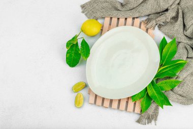 Yaratıcı mutfak konsepti. Boş tabak, olgun limon ve limon, taze yapraklar, modern stand ve eski peçete. Hafif taş zemin, düz zemin, üst manzara