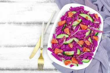 Healthy salad from red Napa cabbage with cucumber, grapefruit, sesame seeds and dressing. Fresh vegetables, delicious food. White wooden background, flat lay, top view clipart