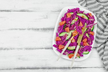 Kırmızı Napa lahanasından sağlıklı salata, salatalık, greyfurt, susam tohumu ve sos. Taze sebzeler, lezzetli yemekler. Beyaz ahşap zemin, düz yatış, üst manzara