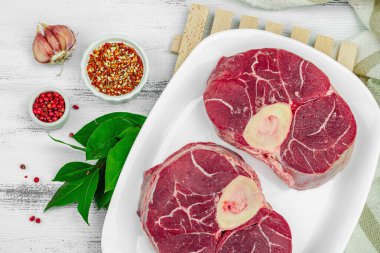Çiğ ossobuco bifteği, baharatlar ve taze otlarla. Dana bifteği, sağlıklı yemek pişirmek için geleneksel İtalyan malzemesi. Beyaz ahşap arkaplan, üst görünüm