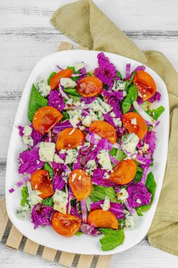 Healthy salad from purple Napa cabbage with persimmon, lettuce, Roquefort cheese and dressing. Fresh vegetables, delicious food. White wooden background, flat lay, top view clipart