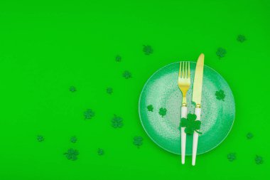 Masa Aziz Patrick Günü konseptini hazırlıyor. El yapımı geleneksel dekoratif semboller, örülmüş leprikon şapka, dört yapraklı yonca, yeşil arka plan, üst manzara.