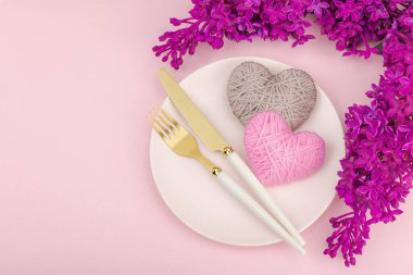 El yapımı kalpleri ve leylak çiçekleri olan yumuşak bahar sofrası. Sevgililer Günü ya da anneler günü, geleneksel bayram sembolü, tebrik kartı. Pastel pembe arkaplan, düz yatış, üst görünüm