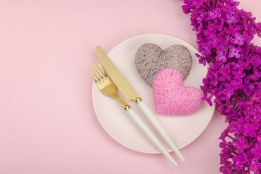 El yapımı kalpleri ve leylak çiçekleri olan yumuşak bahar sofrası. Sevgililer Günü ya da anneler günü, geleneksel bayram sembolü, tebrik kartı. Pastel pembe arkaplan, düz yatış, üst görünüm