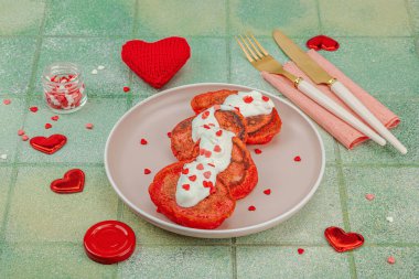 Sevgililer Günü kahvaltısı için tatlı kırmızı gözleme pembe tabakta kalp şeklinde şeker serpiştirilmiş krema. Moda yeşil fayans arkaplanı, kopyalama alanı