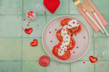 Sevgililer Günü kahvaltısı için tatlı kırmızı gözleme pembe tabakta kalp şeklinde şeker serpiştirilmiş krema. Moda yeşili kaplama arkaplan, üst görünüm