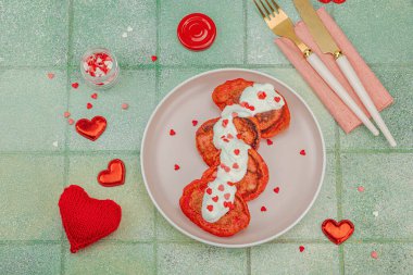 Sevgililer Günü kahvaltısı için tatlı kırmızı gözleme pembe tabakta kalp şeklinde şeker serpiştirilmiş krema. Moda yeşili kaplama arkaplan, üst görünüm