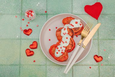 Sevgililer Günü kahvaltısı için tatlı kırmızı gözleme pembe tabakta kalp şeklinde şeker serpiştirilmiş krema. Moda yeşili kaplama arkaplan, üst görünüm