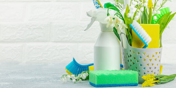 Концепция весенней уборки. Бытовые припасы, бутылки, инструменты и утварь. Традиционные весенние цветы, светлый фон, формат баннера