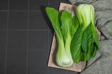 Modayı takip eden siyah fayanslı taze bok choy. Geleneksel Çin lahanası sağlıklı yemek pişirmede kullanılan bir vitamin bileşenidir. Vejetaryen yaşam tarzı, sert ışık, koyu gölge, düz uzanma, üst manzara