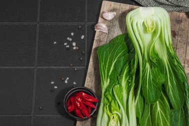 Modayı takip eden siyah fayanslı taze bok choy. Geleneksel Çin lahanası sağlıklı yemek pişirmede kullanılan bir vitamin bileşenidir. Vejetaryen yaşam tarzı, sert ışık, koyu gölge, düz uzanma, üst manzara