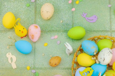 Canlı Paskalya konsepti. Geleneksel bayram sembolleri. Yumurtalar, tavşanlar ve kuşlar. Yaratıcı düz döşeme, yeşil fayans arkaplan, üst görünüm