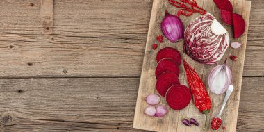 Modern bitki temelli sağlıklı aşçılık tarzı. Düz kırmızı pancar kökü, radicchio, chili biberi, kırmızı soğan, arpacık soğanı ve ahşap arka planda pembe biber, pankart formatı.