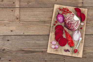 Modern bitki temelli sağlıklı aşçılık tarzı. Düz kırmızı pancar kökü, radicchio, kırmızı biber, kırmızı soğan, arpacık soğanı ve ahşap arka planda pembe biber.