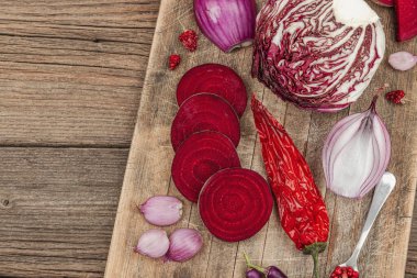 Modern bitki temelli sağlıklı aşçılık tarzı. Düz kırmızı pancar kökü, radicchio, kırmızı biber, kırmızı soğan, arpacık soğanı ve ahşap arka planda pembe biber.