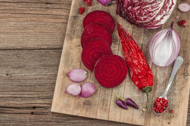 Modern bitki temelli sağlıklı aşçılık tarzı. Düz kırmızı pancar kökü, radicchio, kırmızı biber, kırmızı soğan, arpacık soğanı ve ahşap arka planda pembe biber.