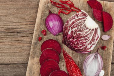 Modern bitki temelli sağlıklı aşçılık tarzı. Düz kırmızı pancar kökü, radicchio, kırmızı biber, kırmızı soğan, arpacık soğanı ve ahşap arka planda pembe biber.