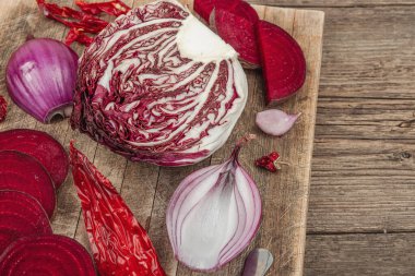 Modern bitki temelli sağlıklı aşçılık tarzı. Düz kırmızı pancar kökü, radicchio, kırmızı biber, kırmızı soğan, arpacık soğanı ve ahşap arka planda pembe biber, yakın plan.