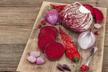 Modern bitki temelli sağlıklı aşçılık tarzı. Düz kırmızı pancar kökü, radicchio, kırmızı biber, kırmızı soğan, arpacık soğanı ve ahşap arka planda pembe biber, kopyalama alanı.