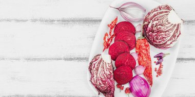 Modern bitki temelli sağlıklı aşçılık tarzı. Düz kırmızı pancar kökü, radicchio, chili biberi, kırmızı soğan, arpacık soğanı ve ahşap arka planda pembe biber, pankart formatı.