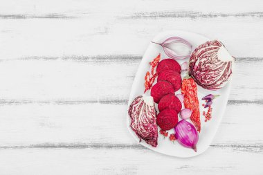 Modern bitki temelli sağlıklı aşçılık tarzı. Düz kırmızı pancar kökü, radicchio, kırmızı biber, kırmızı soğan, arpacık soğanı ve ahşap arka planda pembe biber.