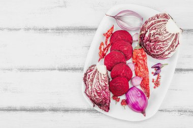 Modern bitki temelli sağlıklı aşçılık tarzı. Düz kırmızı pancar kökü, radicchio, kırmızı biber, kırmızı soğan, arpacık soğanı ve ahşap arka planda pembe biber.