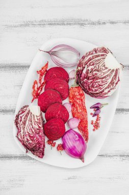 Modern bitki temelli sağlıklı aşçılık tarzı. Düz kırmızı pancar kökü, radicchio, kırmızı biber, kırmızı soğan, arpacık soğanı ve ahşap arka planda pembe biber.