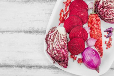 Modern bitki temelli sağlıklı aşçılık tarzı. Düz kırmızı pancar kökü, radicchio, kırmızı biber, kırmızı soğan, arpacık soğanı ve ahşap arka planda pembe biber.