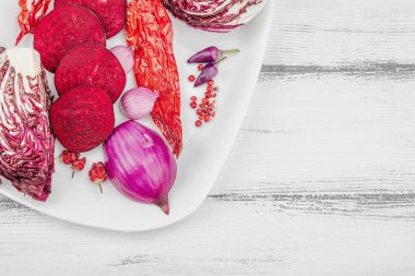 Modern bitki temelli sağlıklı aşçılık tarzı. Düz kırmızı pancar kökü, radicchio, kırmızı biber, kırmızı soğan, arpacık soğanı ve ahşap arka planda pembe biber.