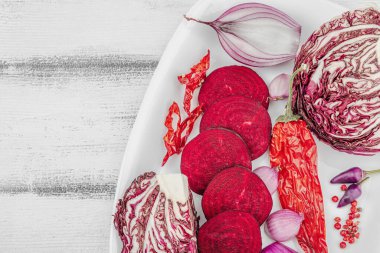 Modern bitki temelli sağlıklı aşçılık tarzı. Düz kırmızı pancar kökü, radicchio, kırmızı biber, kırmızı soğan, arpacık soğanı ve ahşap arka planda pembe biber.