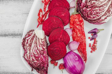 Modern bitki temelli sağlıklı aşçılık tarzı. Düz kırmızı pancar kökü, radicchio, kırmızı biber, kırmızı soğan, arpacık soğanı ve ahşap arka planda pembe biber.