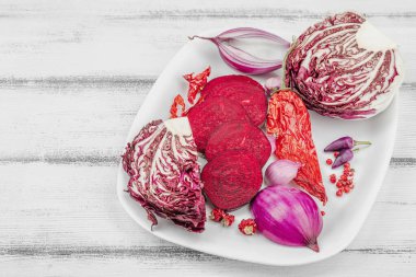 Modern bitki temelli sağlıklı aşçılık tarzı. Düz kırmızı pancar kökü, radicchio, kırmızı biber, kırmızı soğan, arpacık soğanı ve ahşap arka planda pembe biber, kopyalama alanı.