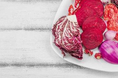 Modern bitki temelli sağlıklı aşçılık tarzı. Düz kırmızı pancar kökü, radicchio, kırmızı biber, kırmızı soğan, arpacık soğanı ve ahşap arka planda pembe biber, kopyalama alanı.