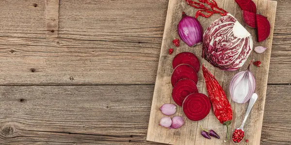 Modern bitki temelli sağlıklı aşçılık tarzı. Düz kırmızı pancar kökü, radicchio, chili biberi, kırmızı soğan, arpacık soğanı ve ahşap arka planda pembe biber, pankart formatı.