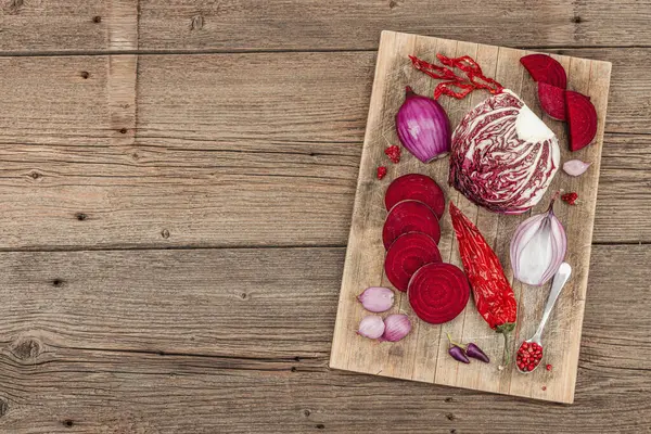 Modern bitki temelli sağlıklı aşçılık tarzı. Düz kırmızı pancar kökü, radicchio, kırmızı biber, kırmızı soğan, arpacık soğanı ve ahşap arka planda pembe biber.