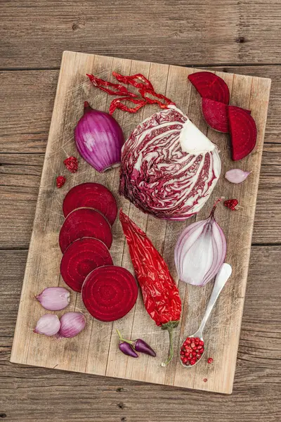 Modern bitki temelli sağlıklı aşçılık tarzı. Düz kırmızı pancar kökü, radicchio, kırmızı biber, kırmızı soğan, arpacık soğanı ve ahşap arka planda pembe biber.