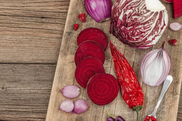 Modern bitki temelli sağlıklı aşçılık tarzı. Düz kırmızı pancar kökü, radicchio, kırmızı biber, kırmızı soğan, arpacık soğanı ve ahşap arka planda pembe biber.
