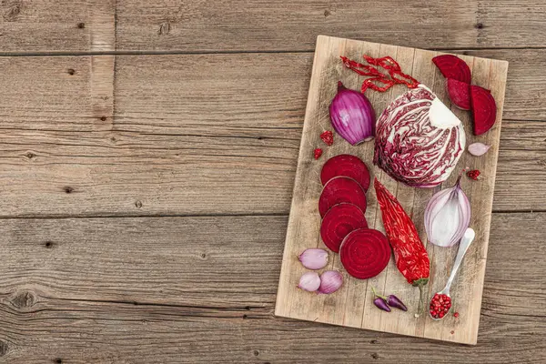 Modern bitki temelli sağlıklı aşçılık tarzı. Düz kırmızı pancar kökü, radicchio, kırmızı biber, kırmızı soğan, arpacık soğanı ve ahşap arka planda pembe biber.