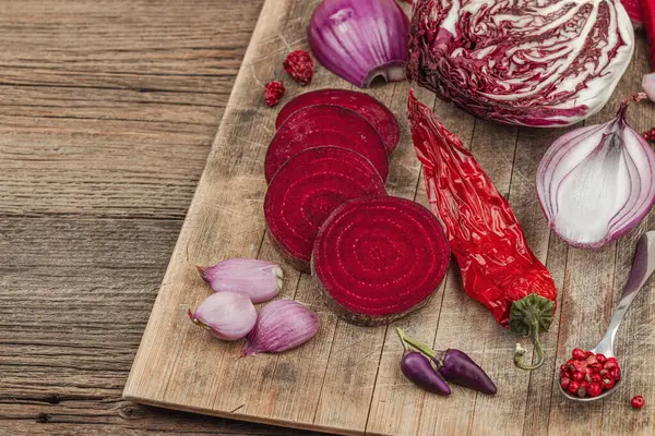 Modern bitki temelli sağlıklı aşçılık tarzı. Düz kırmızı pancar kökü, radicchio, kırmızı biber, kırmızı soğan, arpacık soğanı ve ahşap arka planda pembe biber, kopyalama alanı.