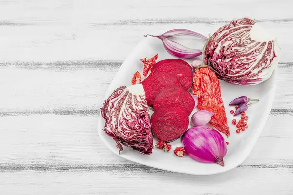 Modern bitki temelli sağlıklı aşçılık tarzı. Düz kırmızı pancar kökü, radicchio, kırmızı biber, kırmızı soğan, arpacık soğanı ve ahşap arka planda pembe biber, kopyalama alanı.