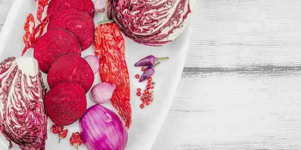 Modern bitki temelli sağlıklı aşçılık tarzı. Düz kırmızı pancar kökü, radicchio, kırmızı biber, kırmızı soğan, arpacık soğanı ve ahşap arka planda pembe biber.