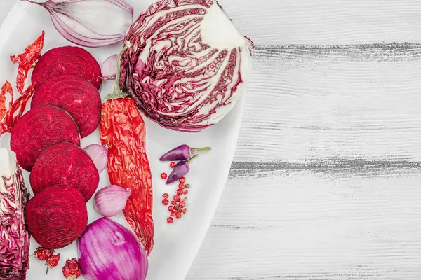 Modern bitki temelli sağlıklı aşçılık tarzı. Düz kırmızı pancar kökü, radicchio, kırmızı biber, kırmızı soğan, arpacık soğanı ve ahşap arka planda pembe biber.