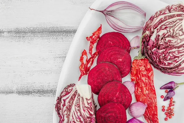 Modern bitki temelli sağlıklı aşçılık tarzı. Düz kırmızı pancar kökü, radicchio, kırmızı biber, kırmızı soğan, arpacık soğanı ve ahşap arka planda pembe biber.