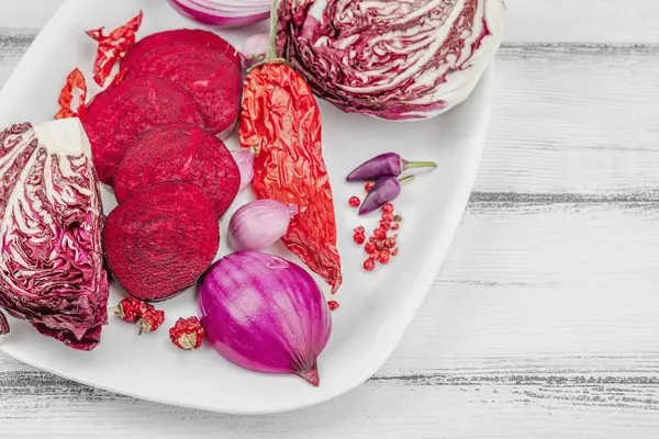 Modern bitki temelli sağlıklı aşçılık tarzı. Düz kırmızı pancar kökü, radicchio, kırmızı biber, kırmızı soğan, arpacık soğanı ve ahşap arka planda pembe biber, kopyalama alanı.
