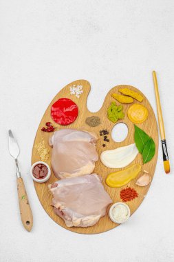 Çiğ tavuk butları, renkli baharatlar ve ahşap bir palette sos ile yaratıcı mutfak konsepti. Aşçıyı gurme mutfağında temsil eden yemek sanatı fikri.